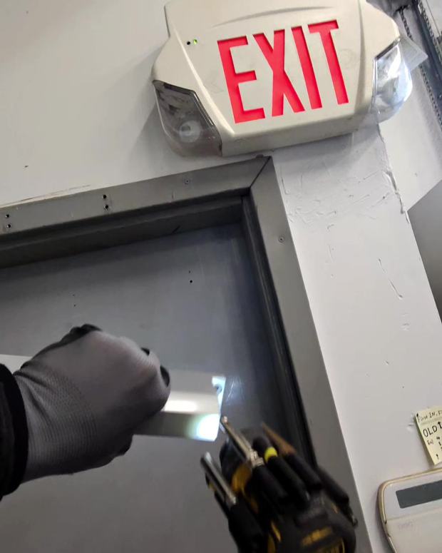 Technician mounting a door closer bracket above a commercial fire-exit door