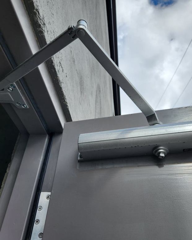 Door closer installed on a grey steel commercial door