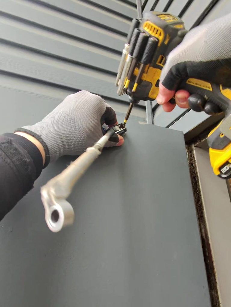 Technician installing a surface-mounted door closer bracket on a grey commercial door with a cordless drill