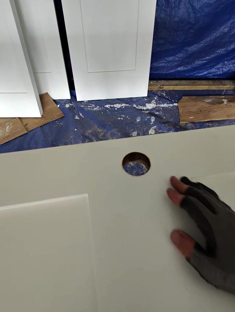 White door slab with a freshly bored lockset hole being prepared in a workshop