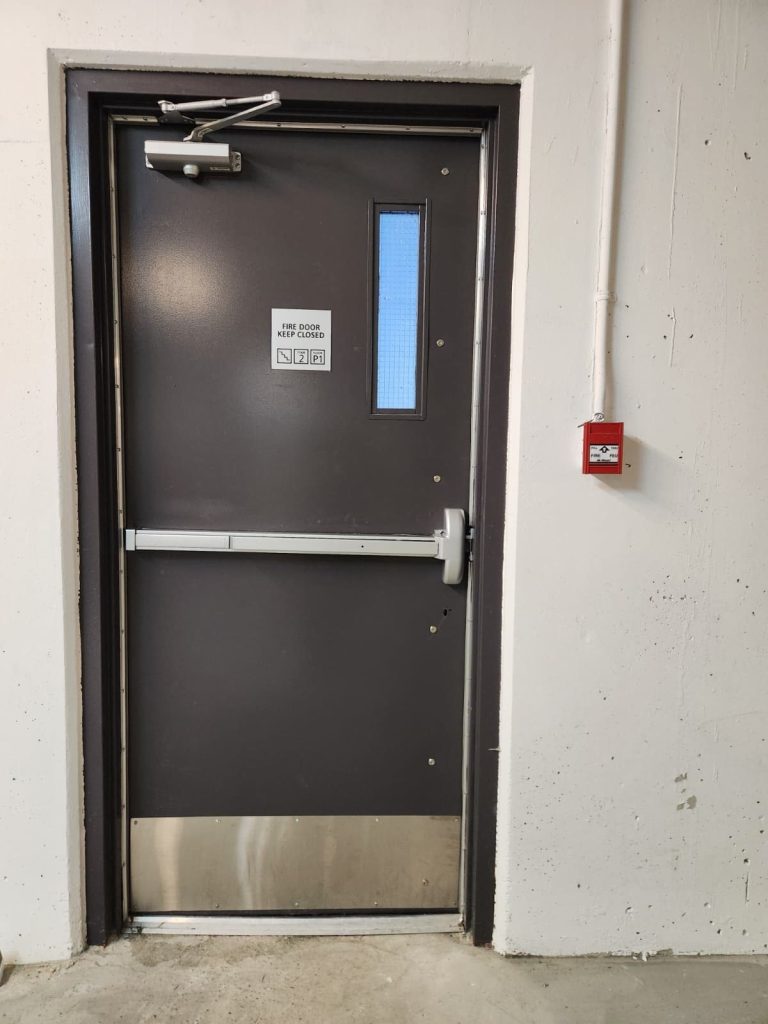 Fire-rated stairwell door with panic exit bar, overhead door closer and stainless kick plate