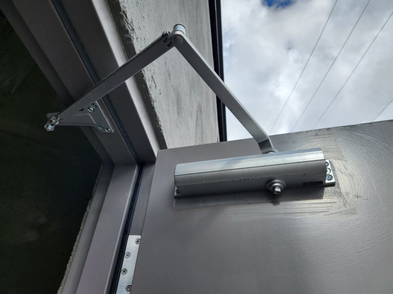 Silver surface door closer with arm installed at the top of a grey exterior metal door
