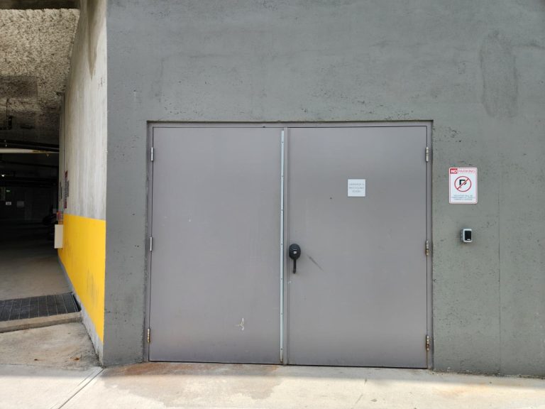 Double grey steel service doors in a parking garage with a wall-mounted access control reader