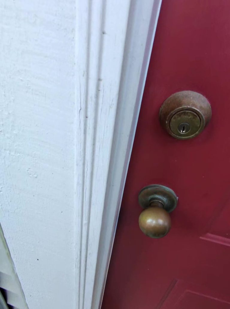 Locksmith working on the brass knob and deadbolt of a red townhouse front door during a lockout call in Vancouver