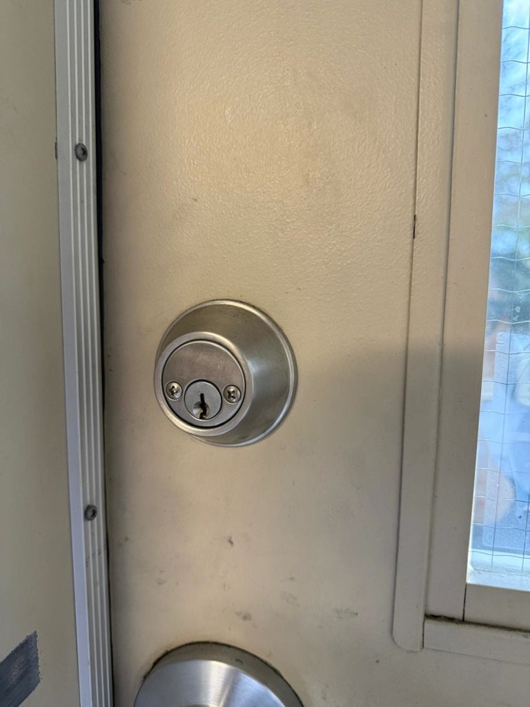 Stainless single-cylinder deadbolt installed in a cream metal entry door next to wired glass