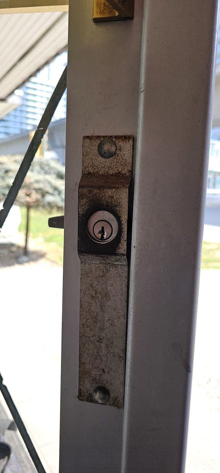 Corroded and worn surface rim lock with cylinder on an aluminum storefront door before replacement